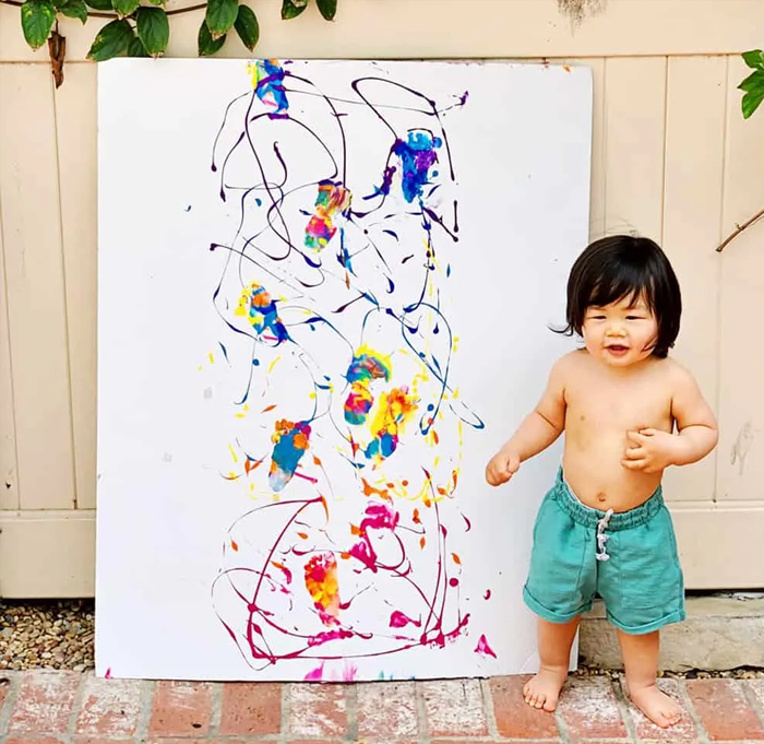 Image shows a toddler enxt to its footprint art work. From Hellowonderful