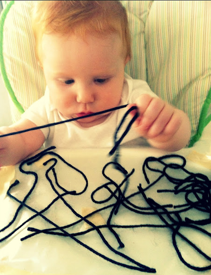 Image shows a toddler playing with yarn. Idea from House of Burke