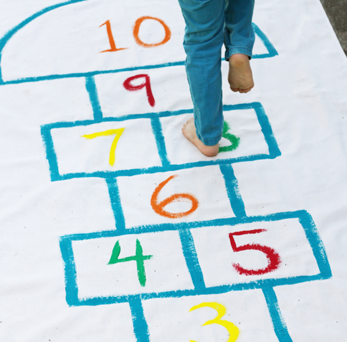 Image shows a kid playing hopscotch. Idea from KAB