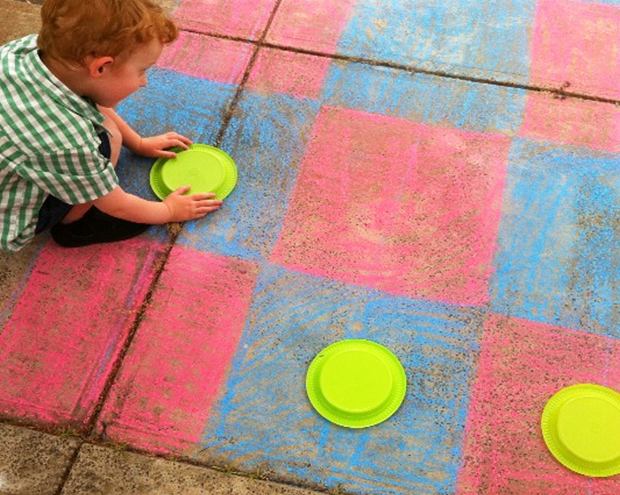 Image shows a kid playing outside with sidewalk chalk and paper plates.