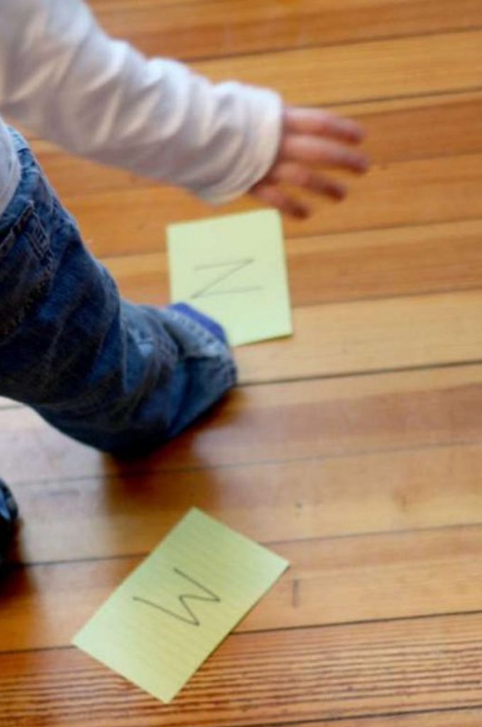 Image shows a toddler playing with letter cards on the floor. From Hands on as we grow