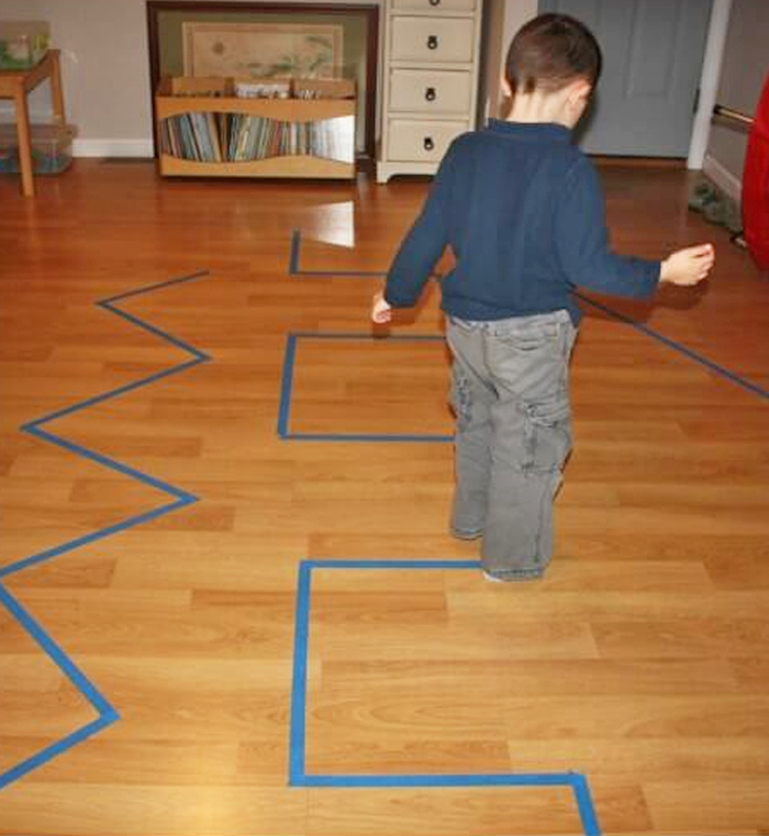 Image shows a toddler playing an indoor activity with tape on the floor. Idea from Little bins 4 little hands.
