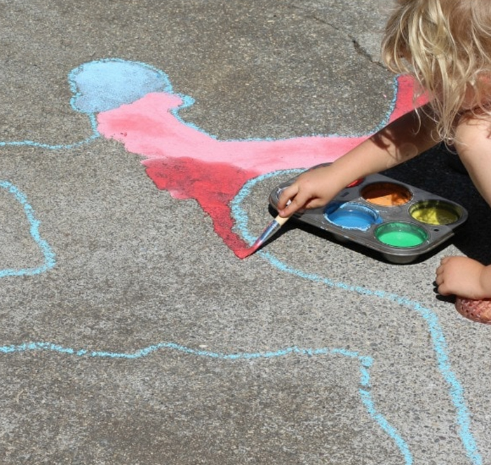 Image shows a kid playing with shadows and chalk outside. Idea from KAB