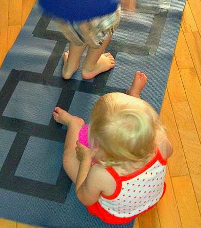 Image shows a toddler and an older kid playing indoor hopscotch game. From The Stay at Home Mom Survival Guide